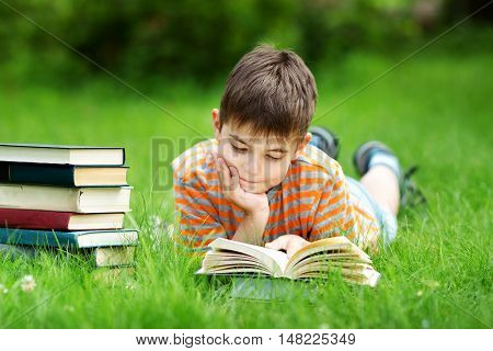 seven years old child reading a book lying on the grass