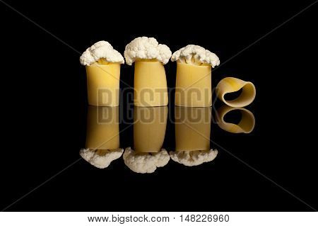 A group of three cauliflowers embedded into pasta manicotti on a black reflection backround