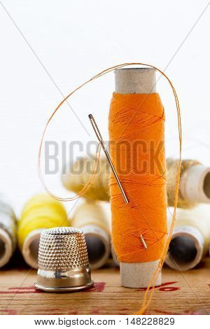 nedle with orange color thread and thimble on the white background