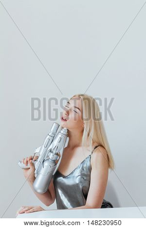 Close up portrait of a beautiful fashion blonde girl in silver shiny dress pointing gun at herself isolated on the grey background