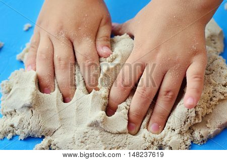 Child playing with kinetic sand. Hands of the child in the sand close up on a bright background