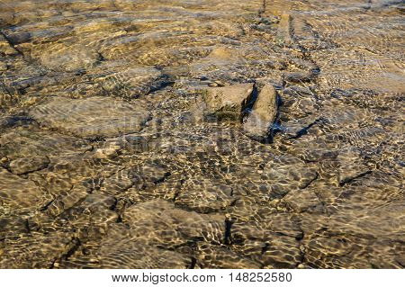 Rippling water with sunbeams and stones in the water