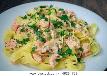Italian Wholemeal Pasta Tagliatelle with Salmon and Parsley. Close up Fresh pasta with smoked salmon in the sauce on old wooden background. Italian cuisine concept. Selective focus.