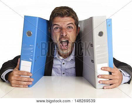 young attractive busy businessman overwhelmed suffering crazy stress at office screaming desperate holding paperwork folders on desk in business frustration and overwork problem