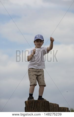 Dancing boy on pedestal. Funny white child with baseball cap. Young lad frolics on stump. Youngster rollicks on music. In captivity of dance. Son spends leisure time activities in music festival.