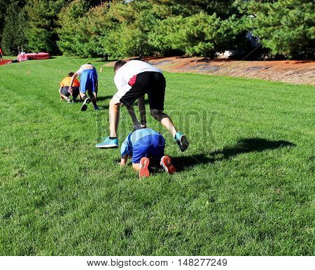 2 teams of teenage boys having a leap frog race on the grass