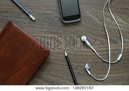 White Headphone, Notebook, Phone And Pencil On Wooden Table