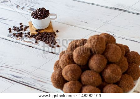 Sweets and coffee beans. White cup on wooden background. Freshly cooked rum balls. Lots of sugar and caffeine.