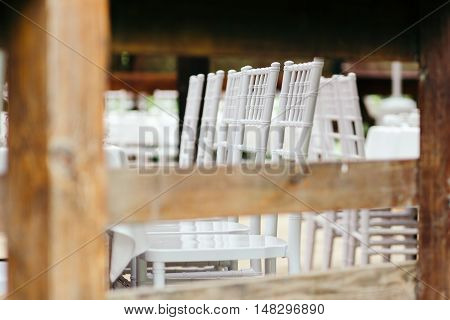 Chiavari chairs on the covered wooden deck. Beautifully arranged, prepared for the ceremony. Shot through a wooden fence.