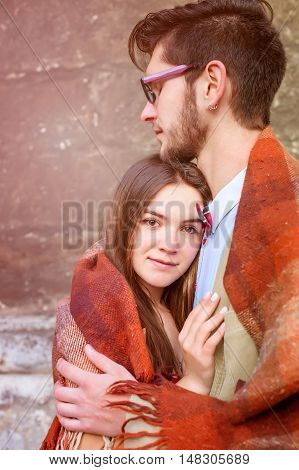 Young fashion elegant stylish couple standing, embracing, wrarps in pled on streets of old european city