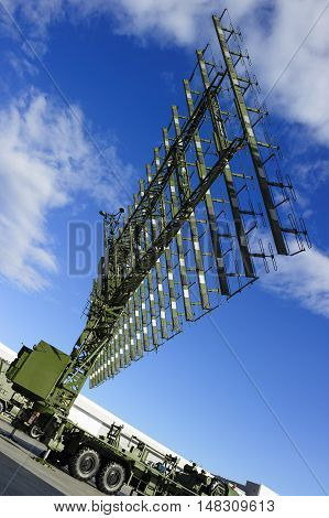 Air defense radar of military mobile antiaircraft system on heavy truck in green color, modern army industry, beautiful clouds and blue sky on background