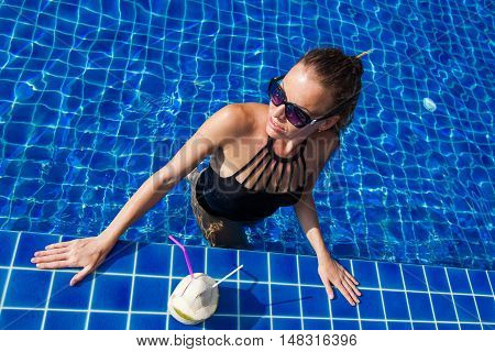 The woman in black swimsuit in blue pool with coconut