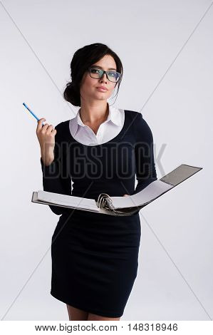 Young Caucasian woman wearing a dark blue dresst and and a white shirt, holding a ring binder folder and pen. Isolated on light background