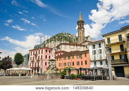 Lecco, Italy - August 17th, 2016: Central streets of Lecco town, with cafe and bell tower. Monument of Mario Cermenati at foreground