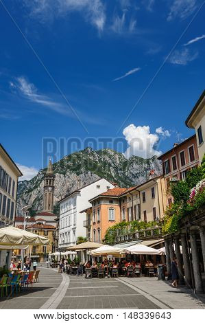 Lecco, Italy - August 17th, 2016: Central streets of Lecco town, with people relaxing in outdoor cafe and bell tower.