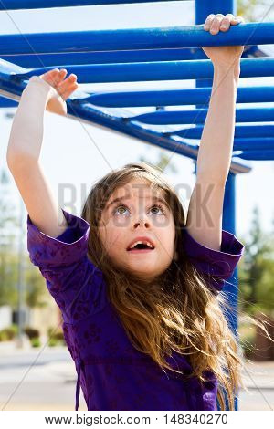 A young girl with a missing front tooth and long brown hair crosses the blue monkey bars at a park playground.