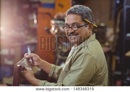 Portrait of smiling shoemaker cutting a piece of leather in workshop