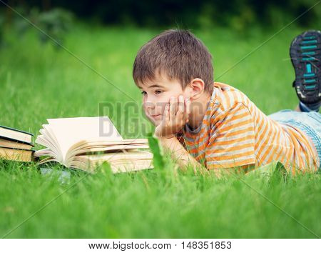 seven years old child reading a book lying on the grass