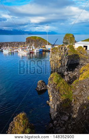 Sunset on the sea fjord in Iceland. White fishing boat in the harbor pier village Arnastapi