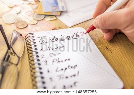 Financial to do list for 2017 - Close-up image with the financial plans for 2017 written by a man's hand in marker on a spiral notebook money cards and bills are in the background.