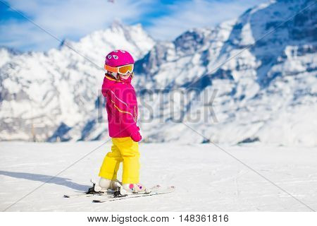 Child skiing in mountains. Active toddler kid with safety helmet goggles and poles. Ski race for young children. Winter sport for family. Kids ski lesson in alpine school. Little skier racing in snow