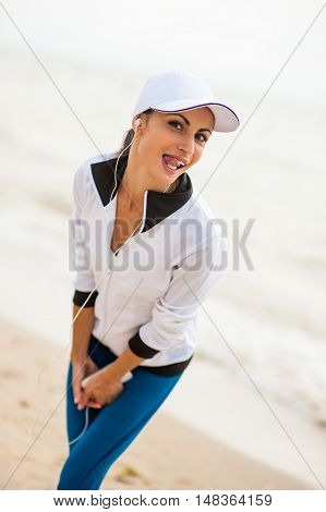 Woman runner running on the beach listening to music on smartphone using earphones. Female fitness girl jogging on path in amazing fall foliage landscape nature outside.