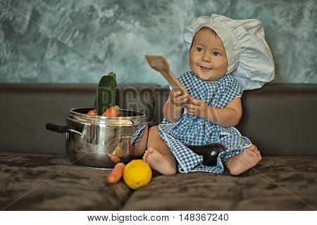 little child dressed as a chef plays with vegetabeles