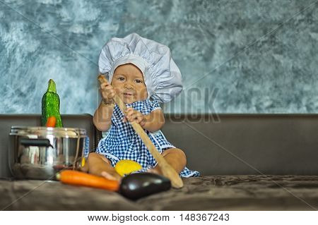little child dressed as a chef plays with vegetabeles