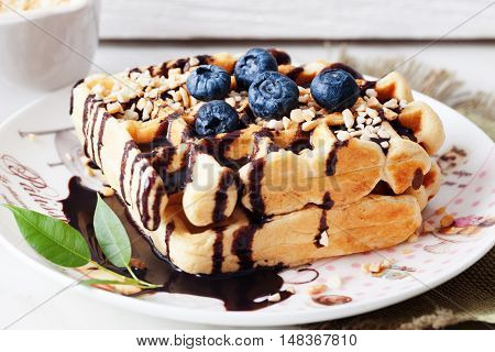 Belgian waffles with peanut chocolate sauce and blueberry bilberry whortleberry huckleberry hurtleberry blaeberry on a plate in still life straw