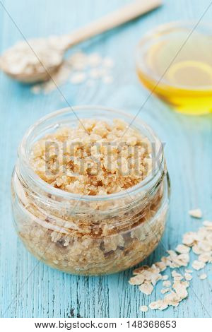 Body scrub of oatmeal sugar, honey and oil in glass jar on blue rustic table. Homemade cosmetic for peeling and spa care, top view.