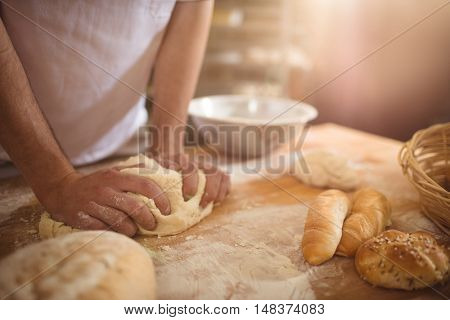 Mid-section of baker kneading a dough in bakery shop