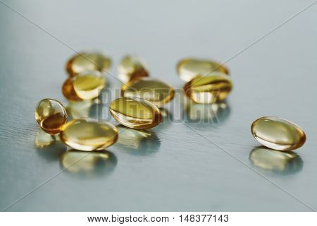 Yellow capsule with vitamin E tocopherol on blue surface, selective focus.