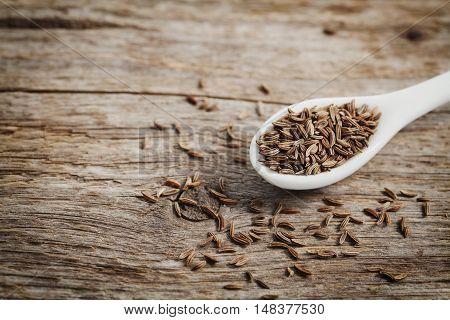 Cumin seeds or caraway in white spoon on wooden board. Macro. Copy space for text.