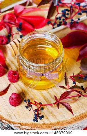 Sweet honey in pot with bow on a wooden background decorated autumn leaves and raspberry. Focus on the front of the pot.