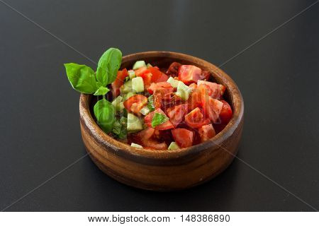 Tomato salad in a wooden bowl decorated with basil leaf