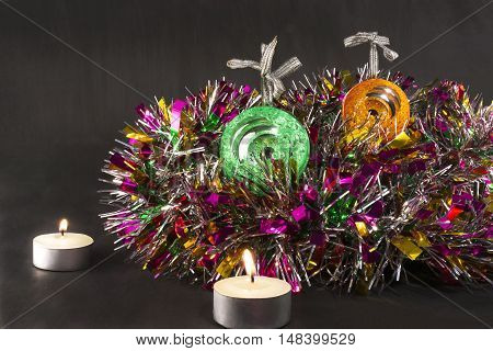 Big green and orange carved mirror xmas balls with a candles on a background of tinsel