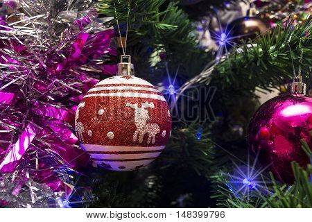 Christmas toys in the form of red ball with deer on the background of tinsel and Christmas tree