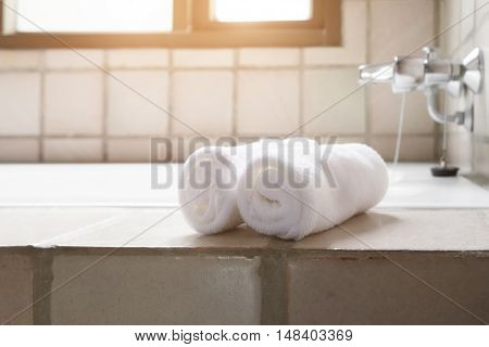 White row of towels beside the bathtub in the bathroom with morning sunlight.
