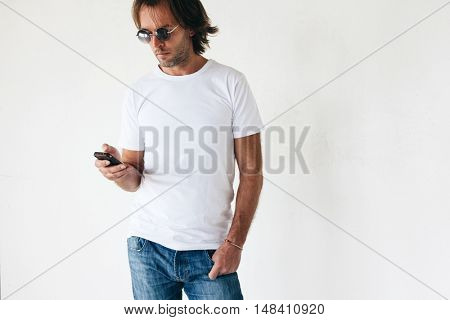 Man wearing blanc t-shirt posing against white wall, toned photo, front tshirt mockup on model