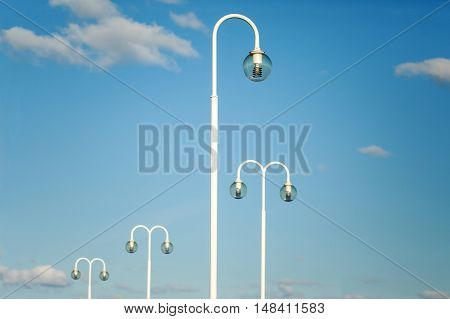 White modern lamp posts against blue sky with clouds. Place for text.