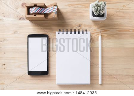 Topview of office stuff on wooden working table. Mock up. Sticky tape note paper white blank notebook post-it note pencil and blank white screen smartphone.