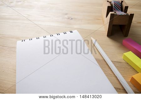Topview of office stuff on wooden working table. Mock up. Sticky tape note paper white blank notebook post-it note pencil.