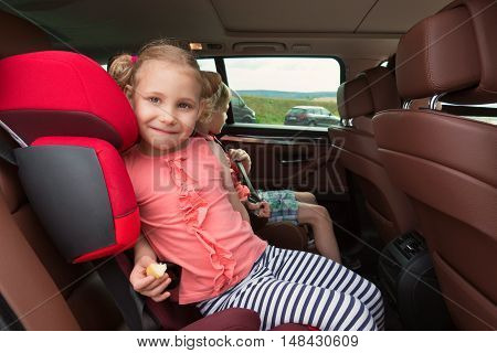 Portrait of happy little child girl sitting comfortable in car seat with safety belts enjoying ride in the auto on family weekend trip