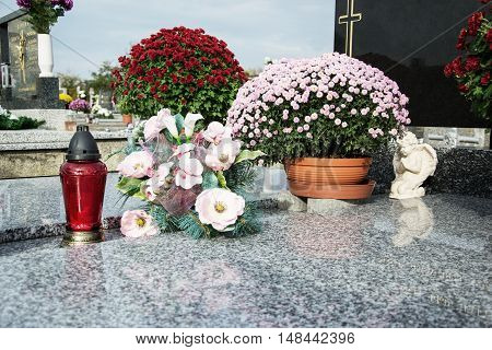 Votive candles lantern and chrysanthemum flowers on tomb stones in graveyard. Graves, tombstones on traditional cemetery. All Saints' Day. All Souls' Day. Gravestones in village Prasice, Slovakia