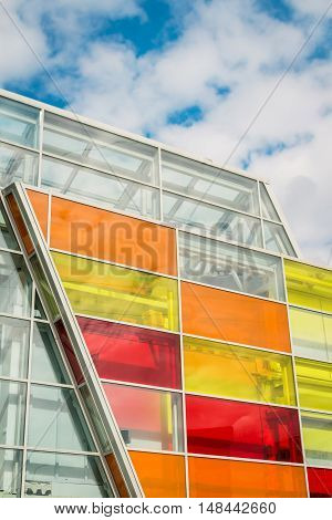 glass facade of a modern building with bright and colorful windows, against the blue sky with clouds