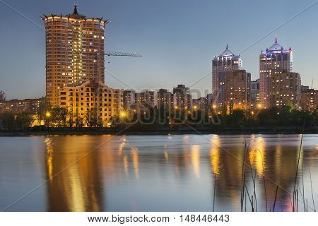 Donetsk City downtown skyline at dusk with skyscrapers illuminated over Kalmius river. Modern skyscrapers. new building construction lights and reflections at water.