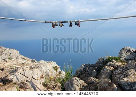 multiple padlocks hung on the metal pipe to the memory on sky background on top of rocky mountain