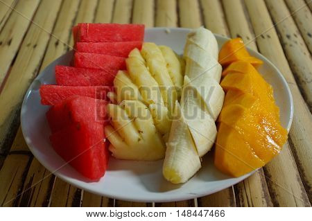 a white plate with sliced fruit: watermelon, mango, banana, pineapple. on the table in a cafe.