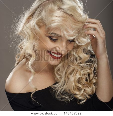 laughing young blond woman modestly looking down in black shirt straightens hair with her hand
