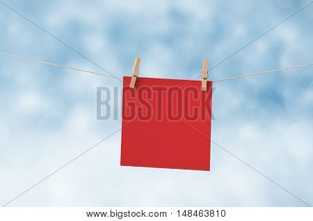 Bllank square of Christmas red paper pegged to a washing line against a blue and white snowy bokeh background.